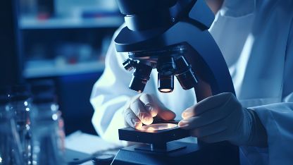 A lab-coated individual studies a sample with a microscope, investigating polymer failure in elastomer seals.