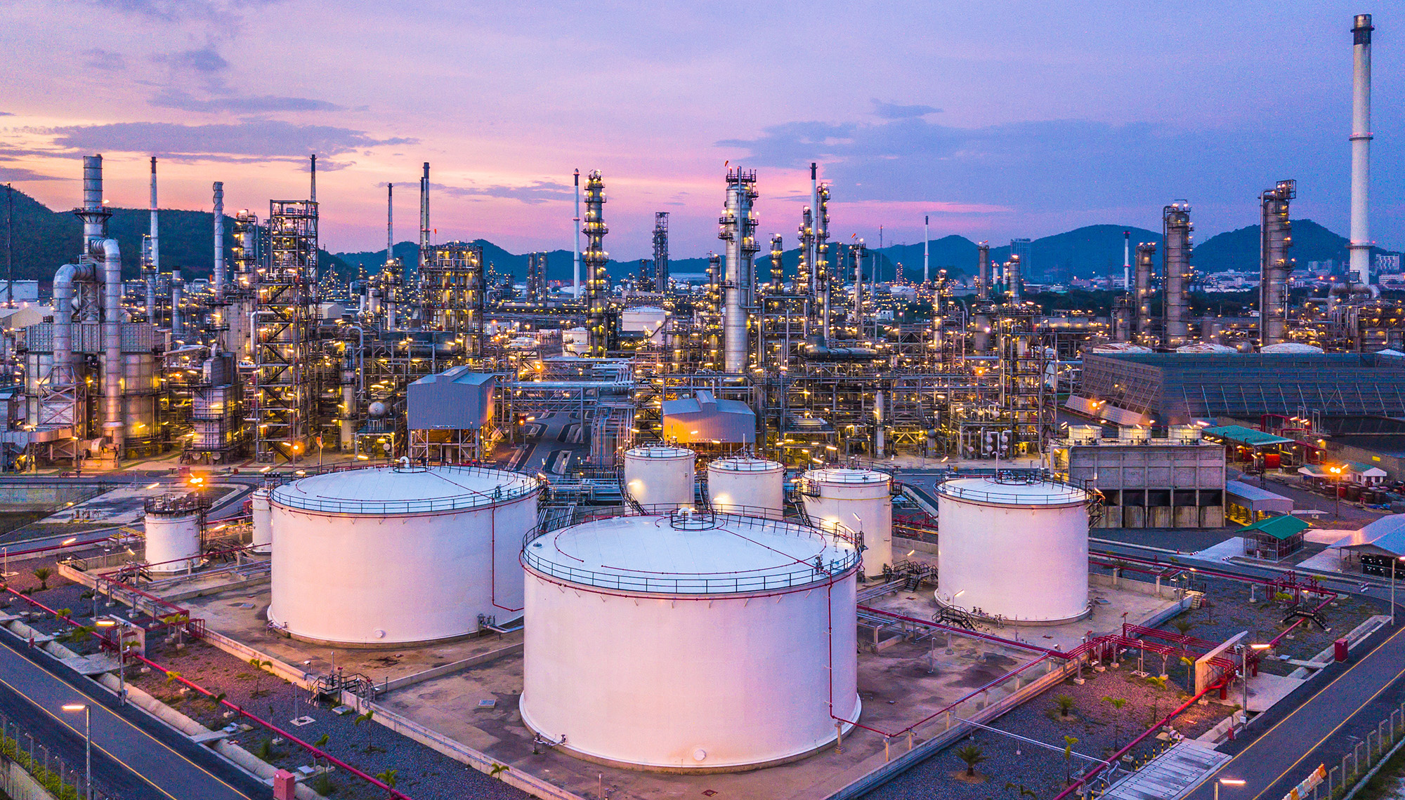 Large refinery showing tanks, towers, lights and mountains in distance