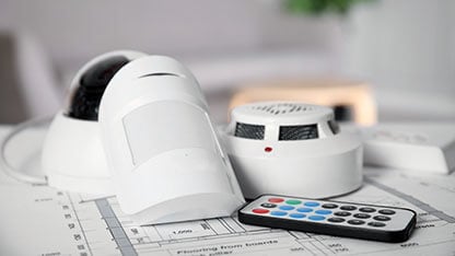 CCTV camera, remote control, smoke and movement detectors on building plan indoors. Home security system 